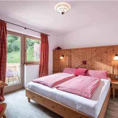 A cozy bedroom with a double bed and wooden paneling. Large windows let in plenty of light and offer a beautiful view of the greenery.