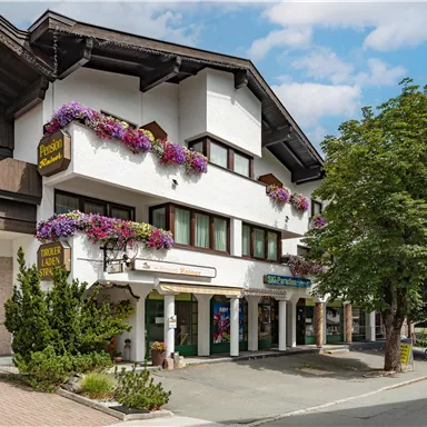 A charming building with blooming flower boxes. It stands on a quiet street, surrounded by trees.