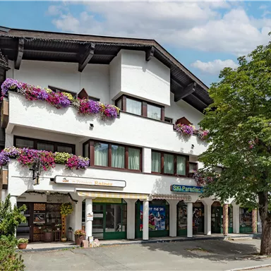 A typical alpine building with blooming balconies. The facade is bright and friendly, surrounded by trees.