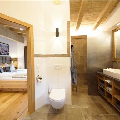 A modern bathroom with elegant design and wooden details. In the background, a comfortable bedroom is visible.