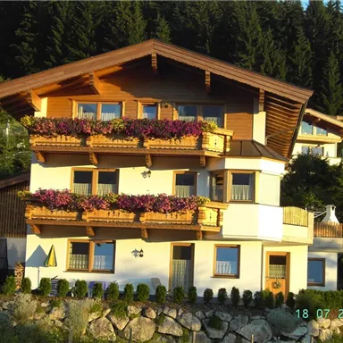 Ein schönes, mehrstöckiges Haus mit einem Holzdach und Blumenkästen. Umgeben von Bäumen und einer grünen Landschaft.