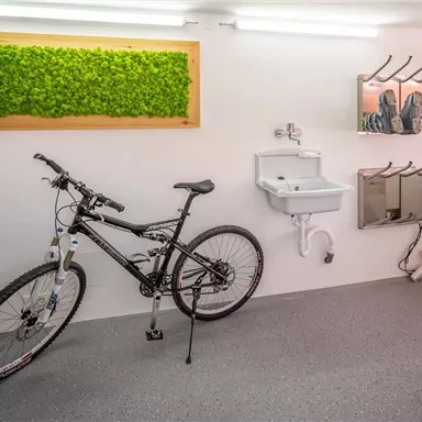 A modern bike garage with a black mountain bike. On the wall, there is a sink and holders for additional accessories.