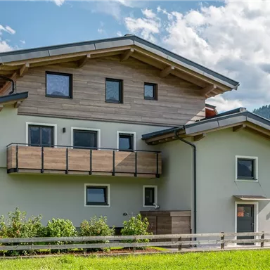 A modern house with wooden cladding and large windows.
Surrounded by green areas and under a clear sky.