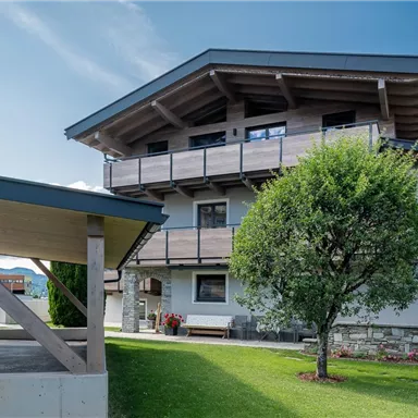 A modern house in the mountains with a green garden. The clear sky and the surrounding landscape create an inviting atmosphere.