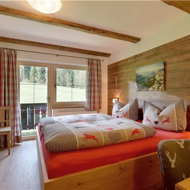 Ein gemütliches Schlafzimmer mit einem großen Bett und Holzmöbeln. Die Fenster bieten einen Blick auf die grüne Landschaft.