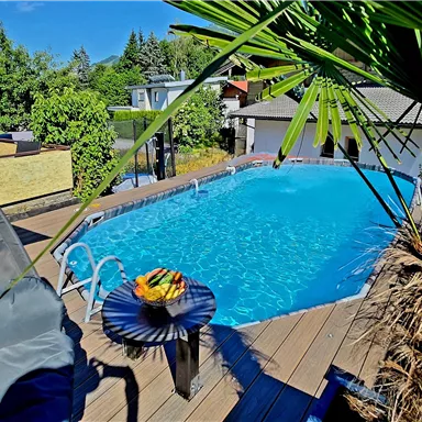 An inviting pool surrounded by plants and a wooden terrace. On the table is a bowl of fresh fruit.