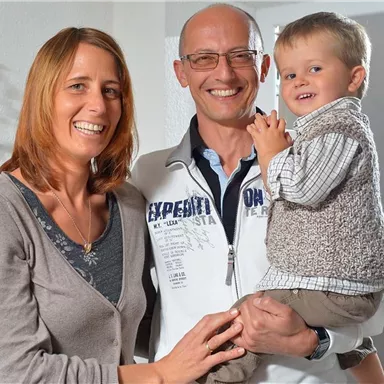 A happy family portrait with a couple and their small child. Everyone is smiling friendly in a bright room.