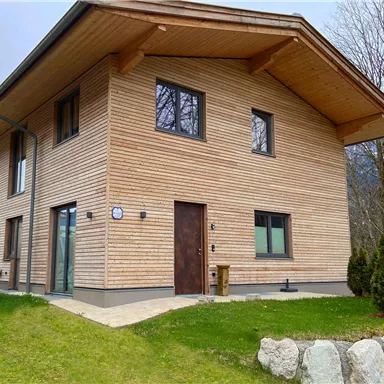 A modern wooden house with an appealing façade. The garden is green and well-kept.