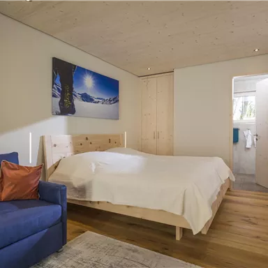 A cozy bedroom with a large bed and a blue couch. On the wall hangs a picture of a snowy landscape.
