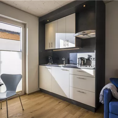 A modern kitchenette with bright furniture and appliances. Next to it stands a table and a chair in a friendly room.