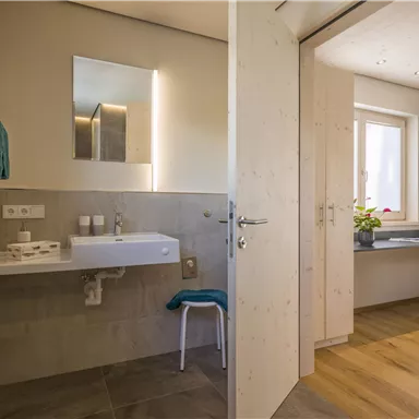 A modern bathroom with bright walls and a small sink. Through the open door, another room with plants is visible.