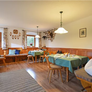 Ein gemütlicher Restaurantbereich mit Holzverkleidung und mehreren Tischen. Das Licht von den Lampen und dem Fenster schafft eine einladende Atmosphäre.