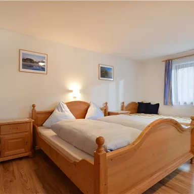Ein gemütliches Schlafzimmer mit zwei Holzbetten und sanfter Beleuchtung. Die Wände sind mit Bildern geschmückt und ein Fenster sorgt für Tageslicht.