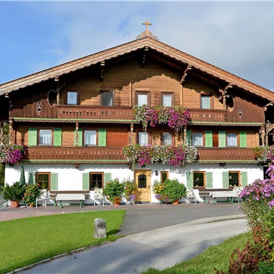 Ein traditionelles alpenländisches Haus mit Holzbalkonen und bunten Blumen. Der Garten ist gepflegt und die Umgebung ist ruhig und malerisch.