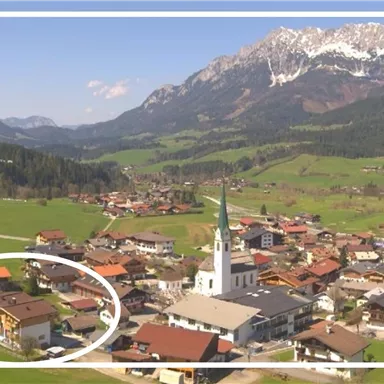 A picturesque village in the mountains with a green landscape and snow-capped peaks in the background. In the foreground stands a striking church, surrounded by traditional buildings.