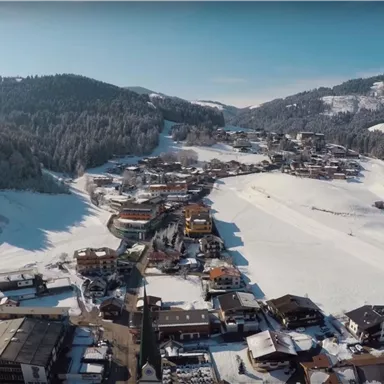 A picturesque mountain landscape with snow-covered hills and a small ski village. The sun shines over the winter scenery and the trees are covered with snow.