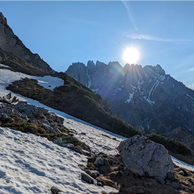 A snowy mountain landscape with steep rocks and shining sunshine. The sky is clear and blue.