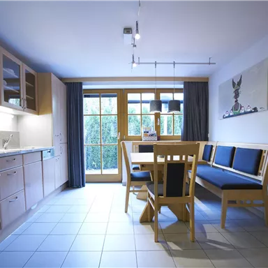 Eine moderne Küche mit einer hellen Essecke. Große Fenster lassen viel Licht herein und bieten einen Blick nach draußen.