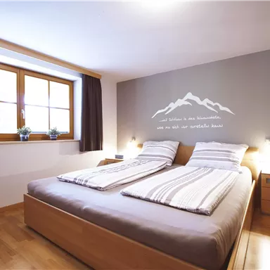 Ein helles Schlafzimmer mit einem Doppelbett und einer gemütlichen Atmosphäre. Fenster mit Blick nach draußen und stilvolle Wanddekoration.
