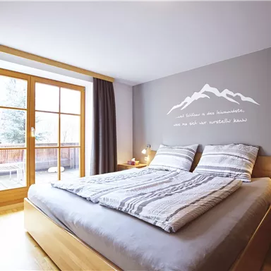 Ein helles Schlafzimmer mit einem großen Bett und Holzdetails. Große Fenster geben einen Blick nach draußen und schaffen eine einladende Atmosphäre.