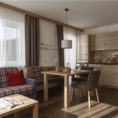 A bright living room with a cozy couch, a table, and a modern kitchenette. Large windows provide plenty of light and a welcoming atmosphere.