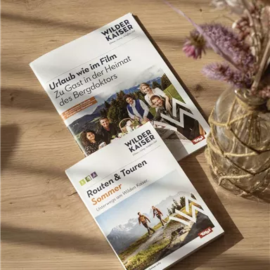 Two brochures on a wooden table. The titles focus on holidays and hikes in the Wilder Kaiser region.