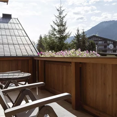 A cozy balcony with a wooden railing and two loungers. In the background, there are mountains and a blue sky.