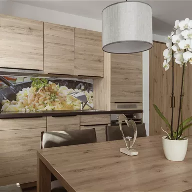 A modern wooden kitchen with a dining table and beautiful orchids. In the background, there is a wall paneling featuring a colorful depiction of food.