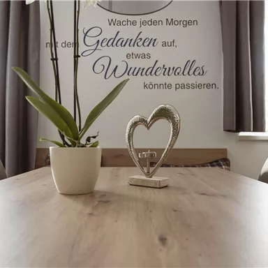 An inviting table with a plant and a decorative heart figure. In the background, there is a phrase on the wall that promotes positive thoughts.