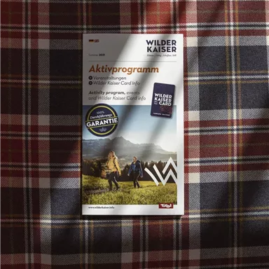 A brochure about the activity program in the Wilder Kaiser area lies on a traditional checked pattern. It showcases activities in nature and provides practical information for visitors.