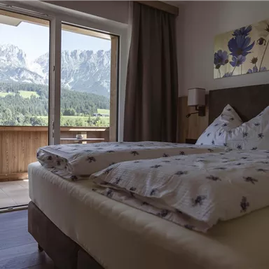 A cozy bedroom with a double bed and a beautiful view of the mountains. Large windows provide access to a balcony overlooking nature.