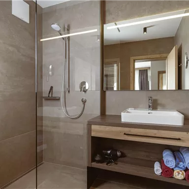 A modern bathroom with a spacious shower and an elegant sink. Colorful towels are neatly arranged on a wooden shelf.