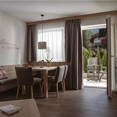 A cozy living room with a dining area and large windows. The room has a warm, inviting wood look and access to a terrace.