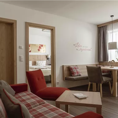 A cozy living space with red plaid sofas and a wooden table. The room is bright and inviting, with a large window that lets in daylight.