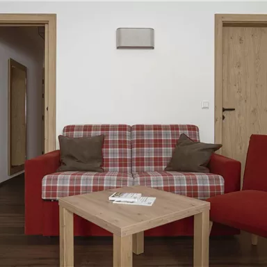 A cozy living room with a red sofa and a red armchair. The wooden table complements the friendly atmosphere of the room.