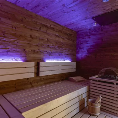 A modern sauna with wooden cladding and soft, purple lighting. The benches are made of light wood and create a relaxing atmosphere.