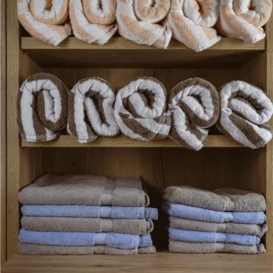 Rolled towels on a wooden shelf. The colored towels are neatly stacked and create a cozy atmosphere.
