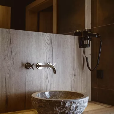 A modern bathroom with an elegant stone washbasin and a stylish faucet. The walls are in warm wood tones, creating a cozy atmosphere.