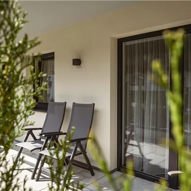 A cozy terrace with two loungers and large windows. The surroundings are adorned with plants.