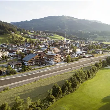 A picturesque landscape with a small village in the valley and gentle hills in the background. The road and a golf course are also visible.