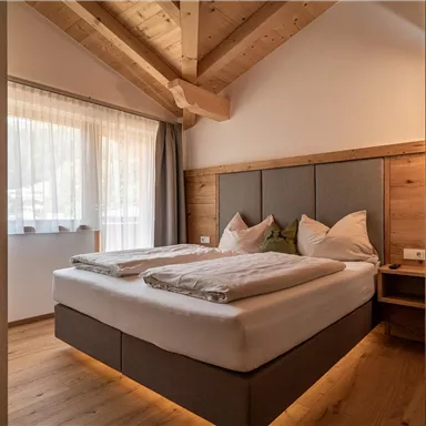 A cozy bedroom with a large bed and wooden elements. Bright windows create a friendly atmosphere.