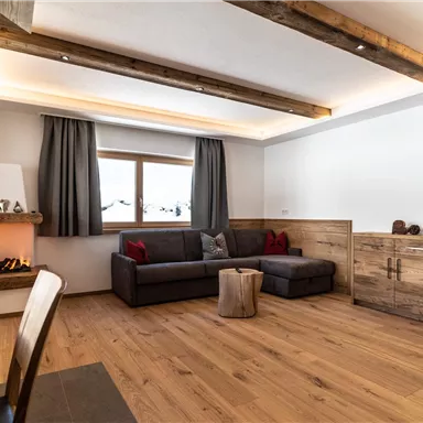 A cozy living room with a modern sofa and wooden floor. The windows are adorned with curtains, and a fireplace creates a pleasant atmosphere.