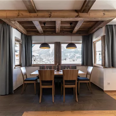 A modern dining room with wooden ceilings and large windows. There is a table with chairs and a bright, inviting atmosphere.