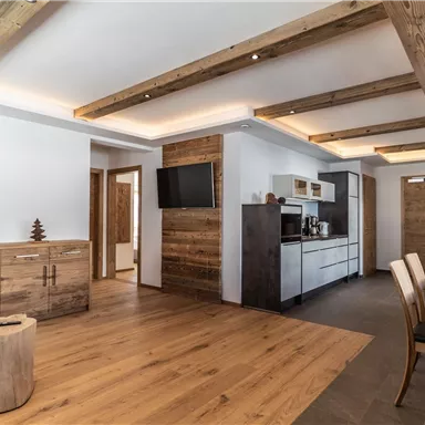A modern living room with wooden beams and wooden flooring. There is a small kitchen and a dining table set.