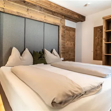 A cozy bedroom with a large bed and a modern wooden wall. The room is bright and minimally furnished.