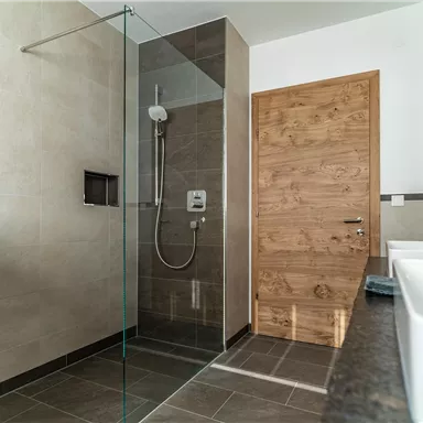 A modern bathroom with a glass shower cabin and elegant design. The bright walls and the wood tone of the door create a pleasant atmosphere.