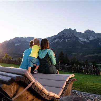 A family is sitting on a bench and looking at the majestic mountains during sunset. The scene radiates tranquility and a connection with nature.