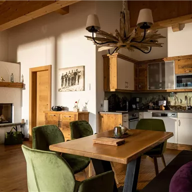 A cozy living room with a wooden table and colorful chairs. The modern kitchen and the fireplace create an inviting atmosphere.
