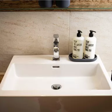 A modern sink with simple care products. The surface is bright and stylish, surrounded by wood and stone.