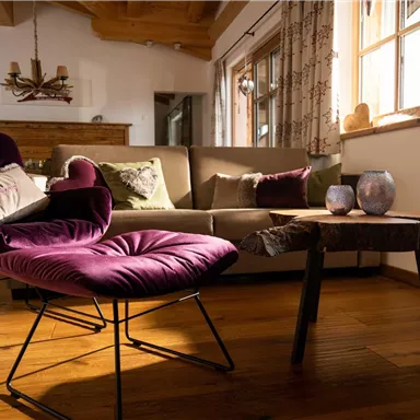 A stylishly furnished room with a purple armchair and a small wooden table. The windows let in plenty of daylight, creating an inviting atmosphere.